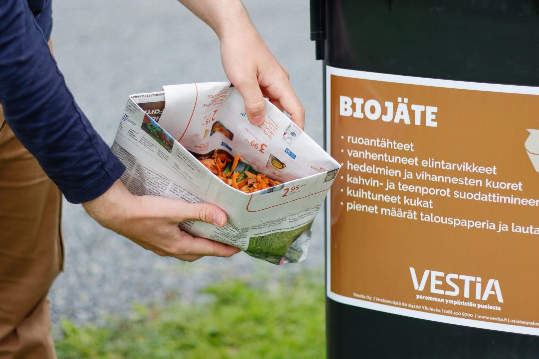 Biojätteitä sanomalehdistä tehdyssä pussissa ja biojäteastia Vestian ohjetarralla