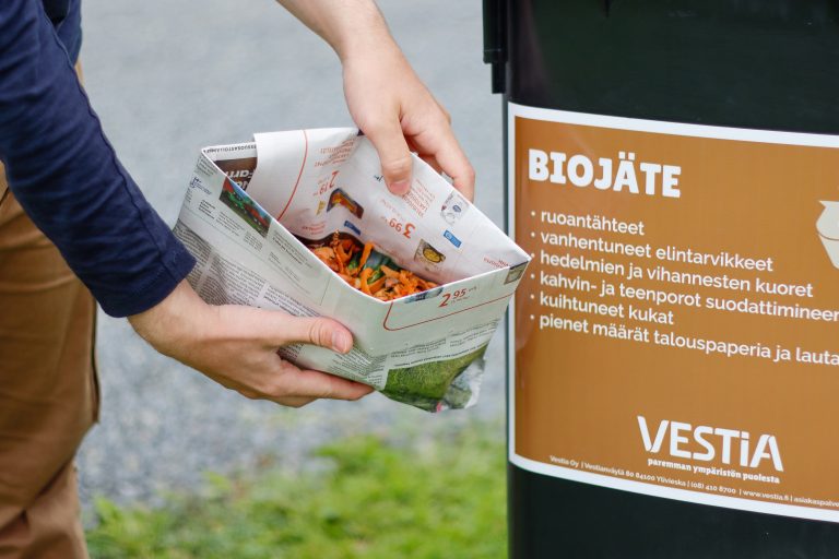 Biojätteitä sanomalehdistä tehdyssä pussissa ja biojäteastia Vestian ohjetarralla